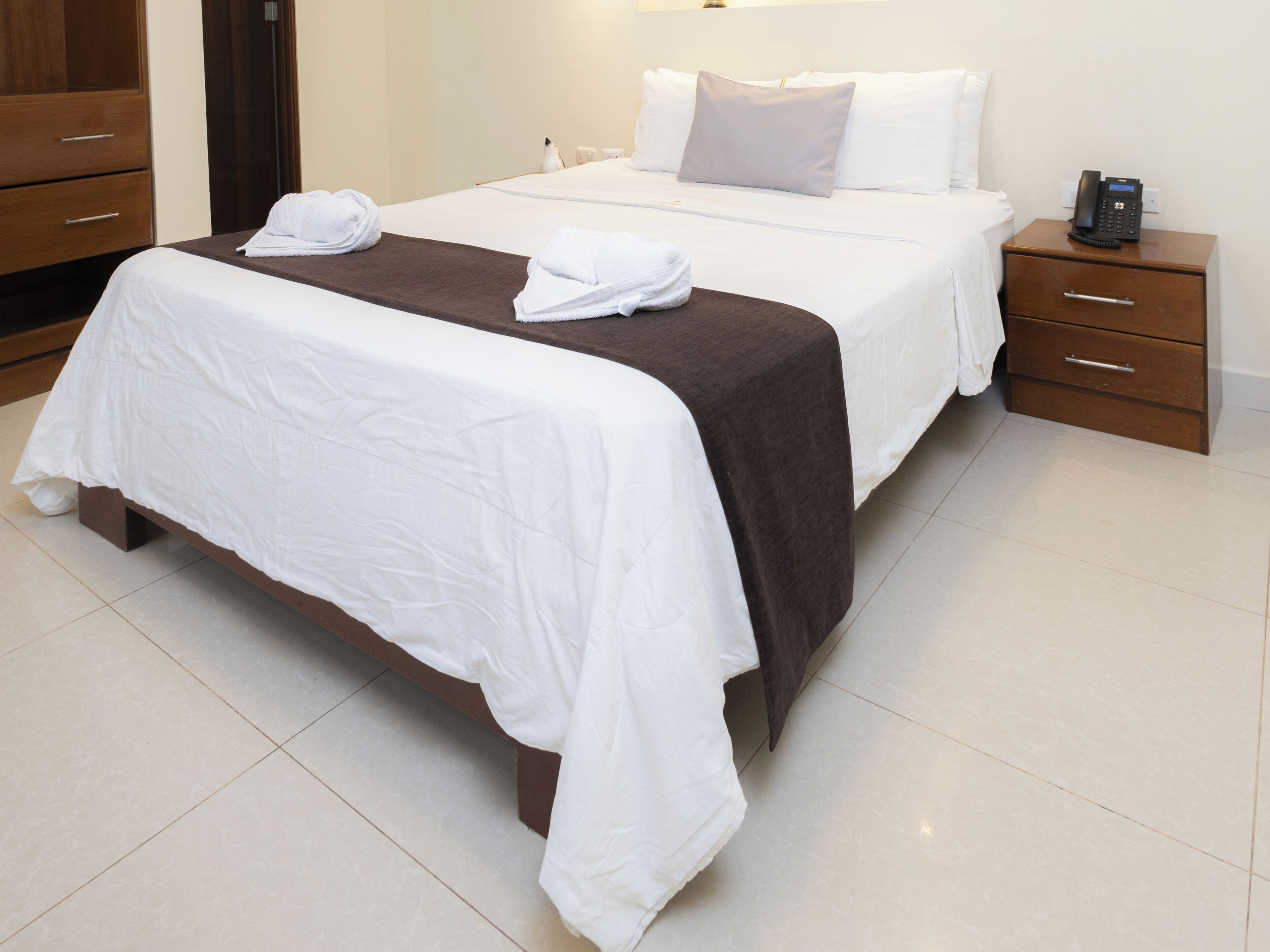 A hotel room with two beds, a nightstand with a phone, and a wooden wardrobe.
