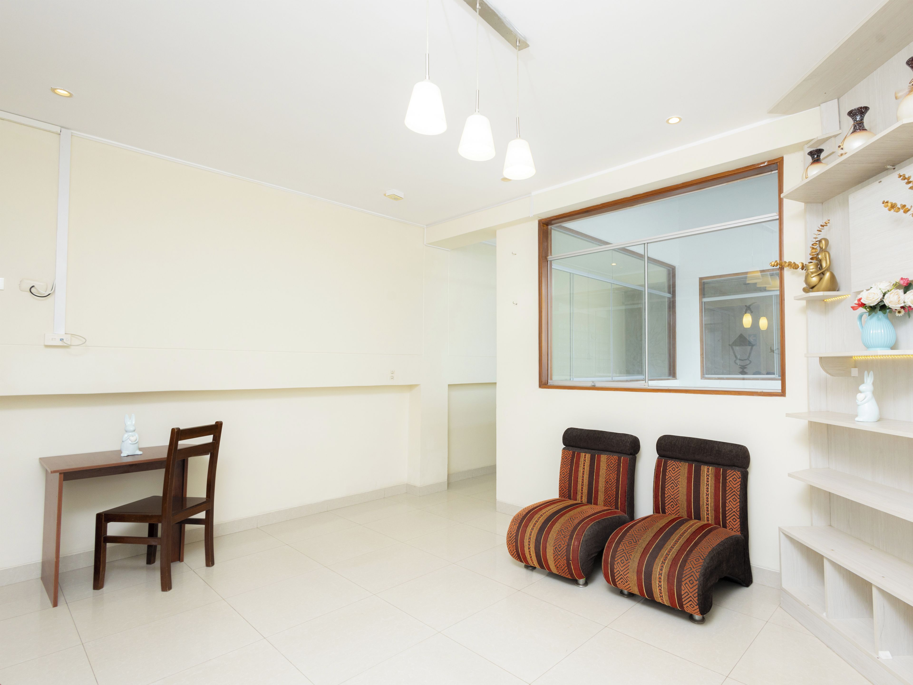 Una habitación moderna con una mesa de comedor, dos sillas, un sofá, un espejo grande y una estantería con objetos decorativos.
