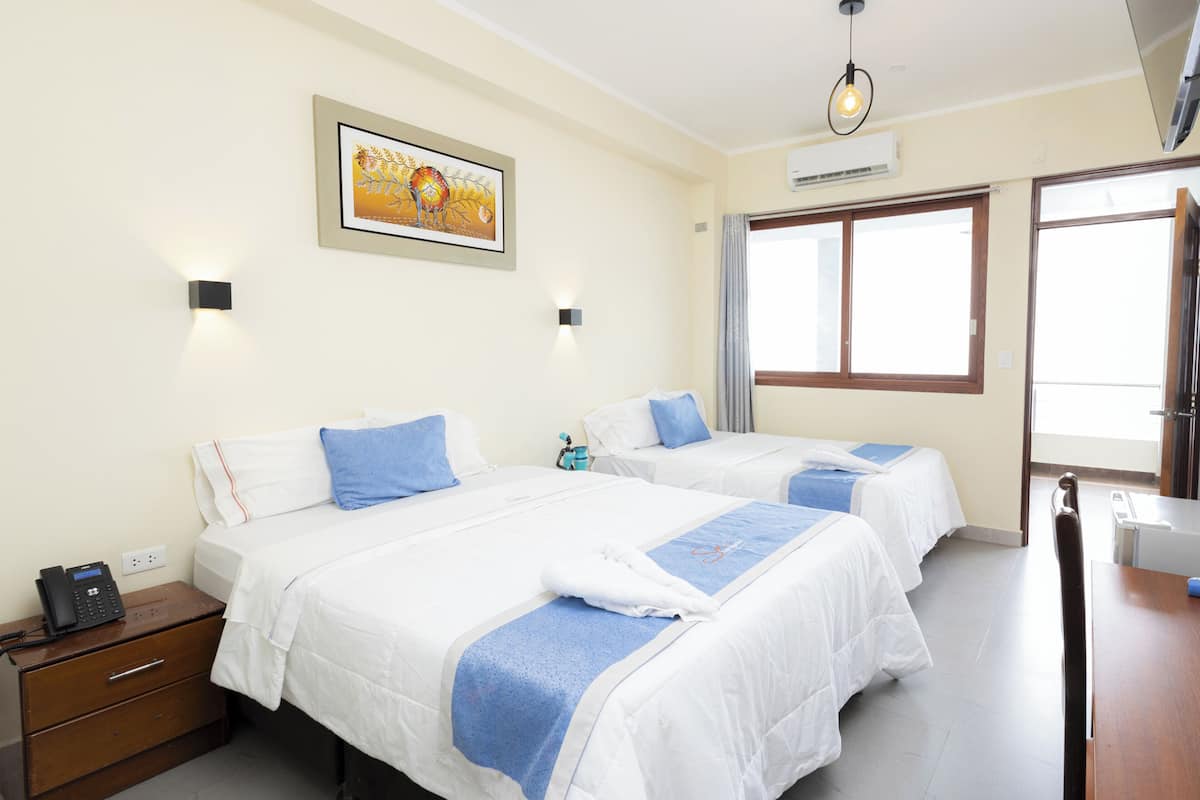 Habitación de hotel con dos camas, una mesita de noche de madera, un teléfono, un cuadro en la pared y una ventana con cortinas.