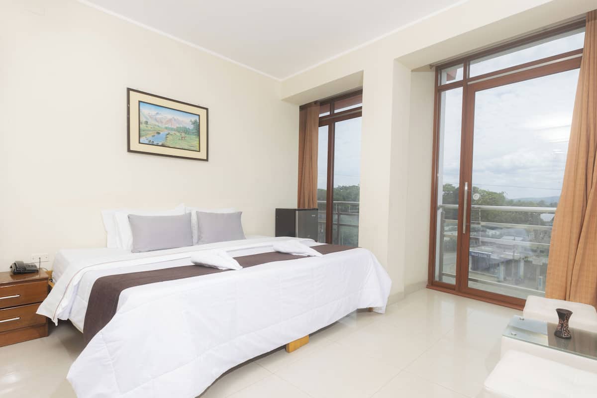 Una habitación de hotel con una cama grande, un escritorio, una silla, un ventanal con vistas y un cuadro en la pared.