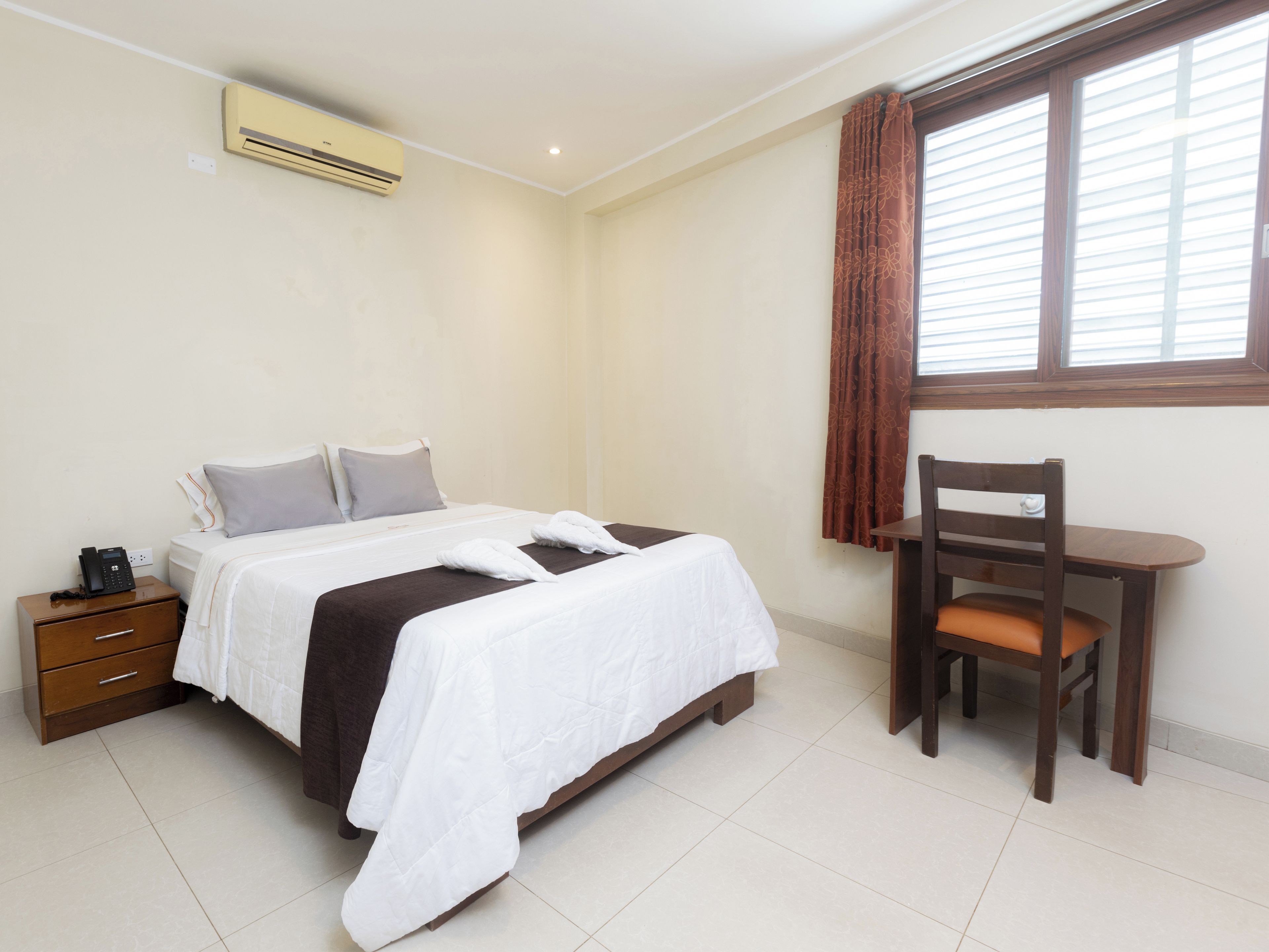 A hotel room with a bed, bedside table, chair, and window with curtains.