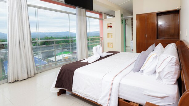 Habitación de hotel con una cama grande, televisión, armario y balcón con vistas a las montañas.