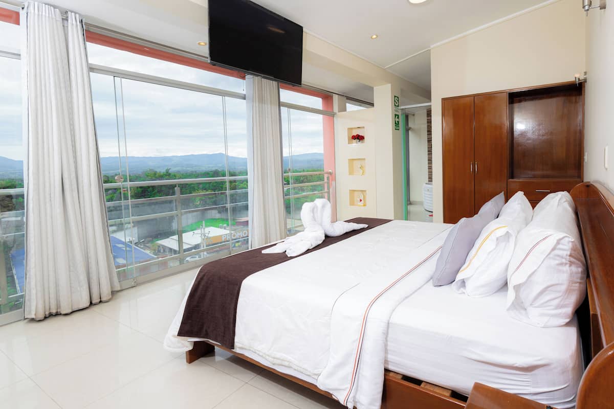 Habitación de hotel con una cama grande, televisión, armario y balcón con vistas a las montañas.