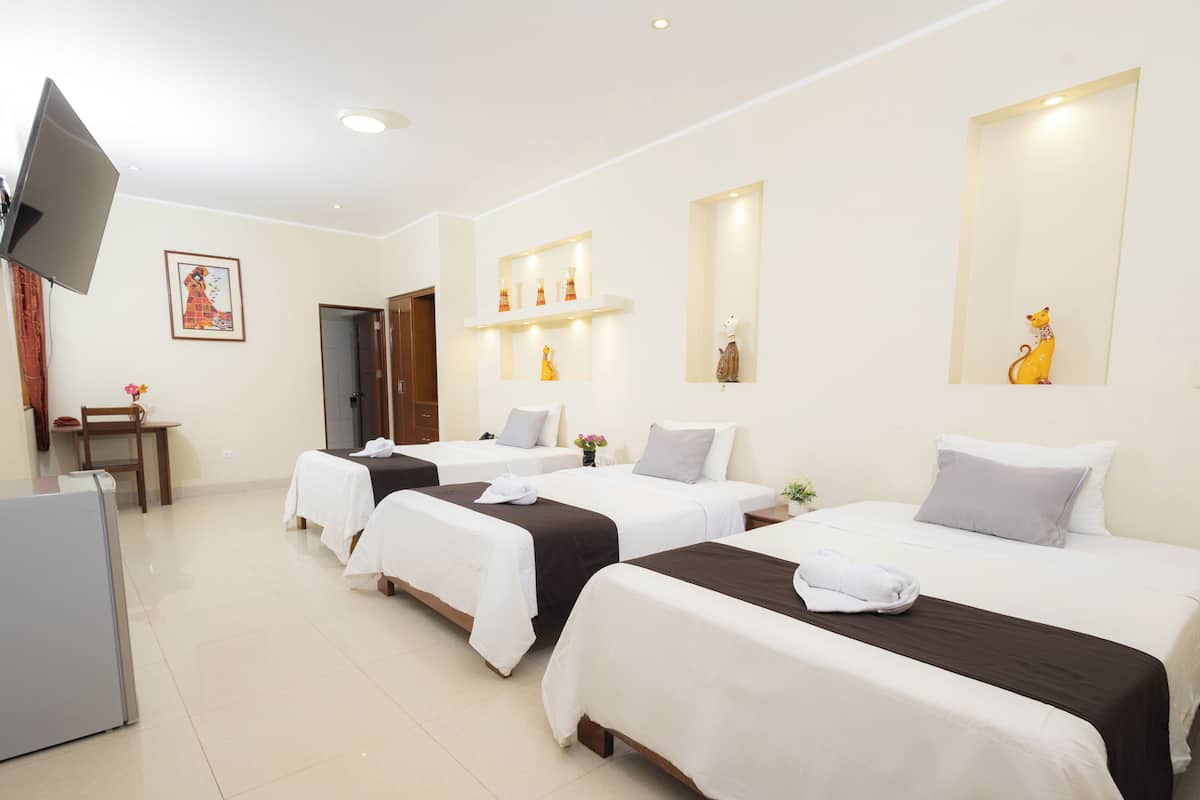 Habitación de hotel con cuatro camas individuales, un televisor, un escritorio y una silla.