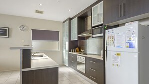 A modern kitchen with dark cabinetry, a white refrigerator with magnets, a microwave, and a built-in oven. - The Cove, Port Hughes (Port Hughes)