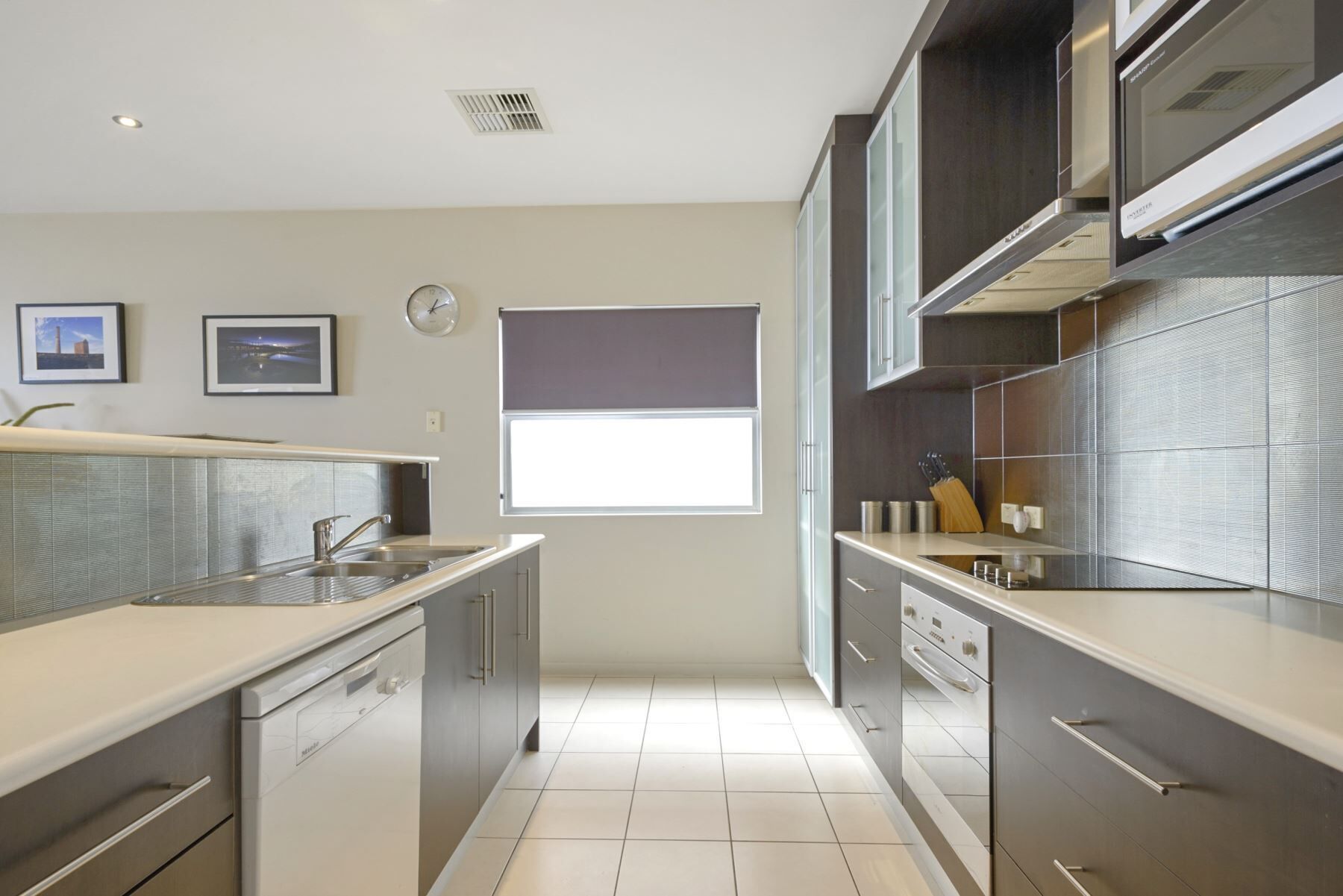 A modern kitchen with stainless steel appliances, a window, and a clock on the wall.