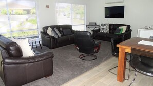 A modern living room with leather sofas, a wooden dining table, and a flat-screen TV mounted on the wall.