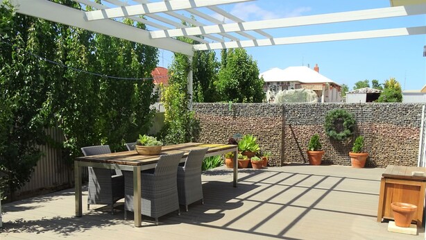 An outdoor patio with a pergola, a dining table with chairs, and potted plants.