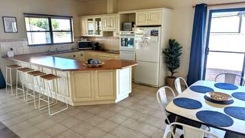 A modern kitchen with a large island, bar stools, a dining table with placemats, and a refrigerator.