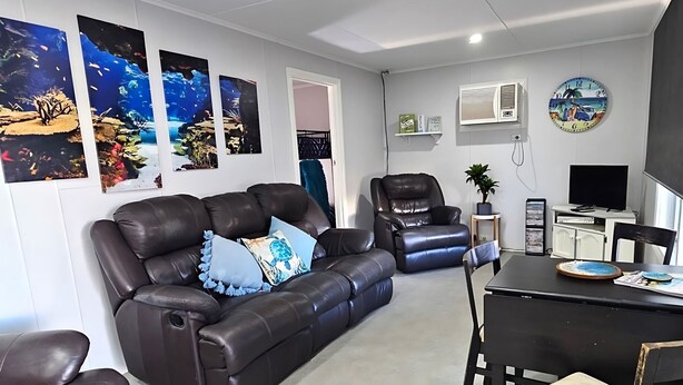 Un salon avec un canapé en cuir marron, un fauteuil en cuir noir, une table à manger avec des chaises, un téléviseur et un climatiseur fixé au mur.