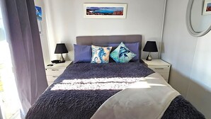 Une chambre à coucher avec un grand lit, deux tables de chevet, une lampe sur chacune, et un tableau encadré au mur.