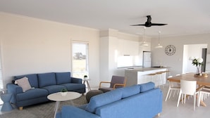 A modern living room with a blue sofa, a round coffee table, and a dining area with a wooden table and white chairs.