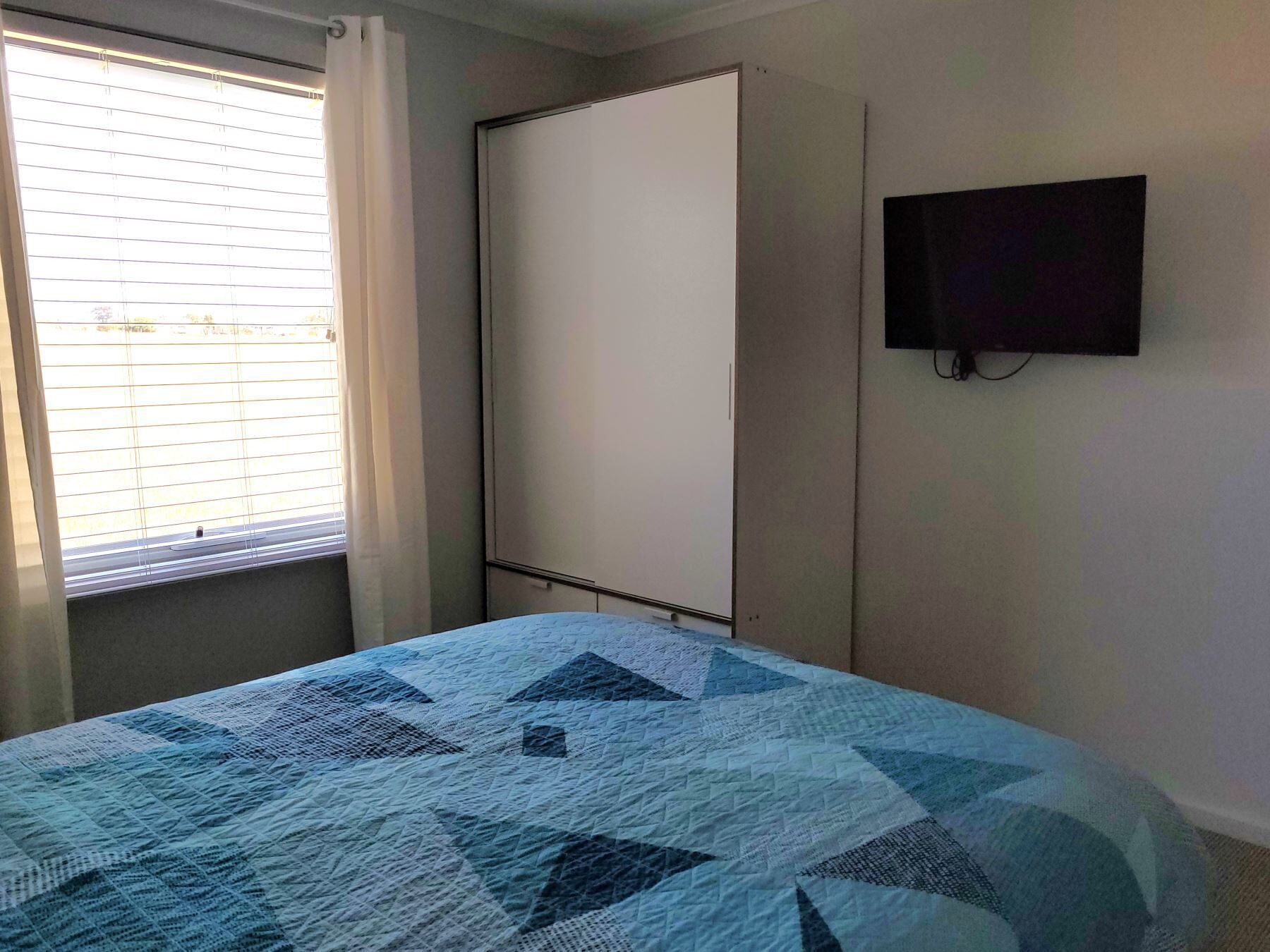 Ein Schlafzimmer mit einem Bett, einem Kleiderschrank, einem Fernseher und einem Fenster mit Jalousien.
