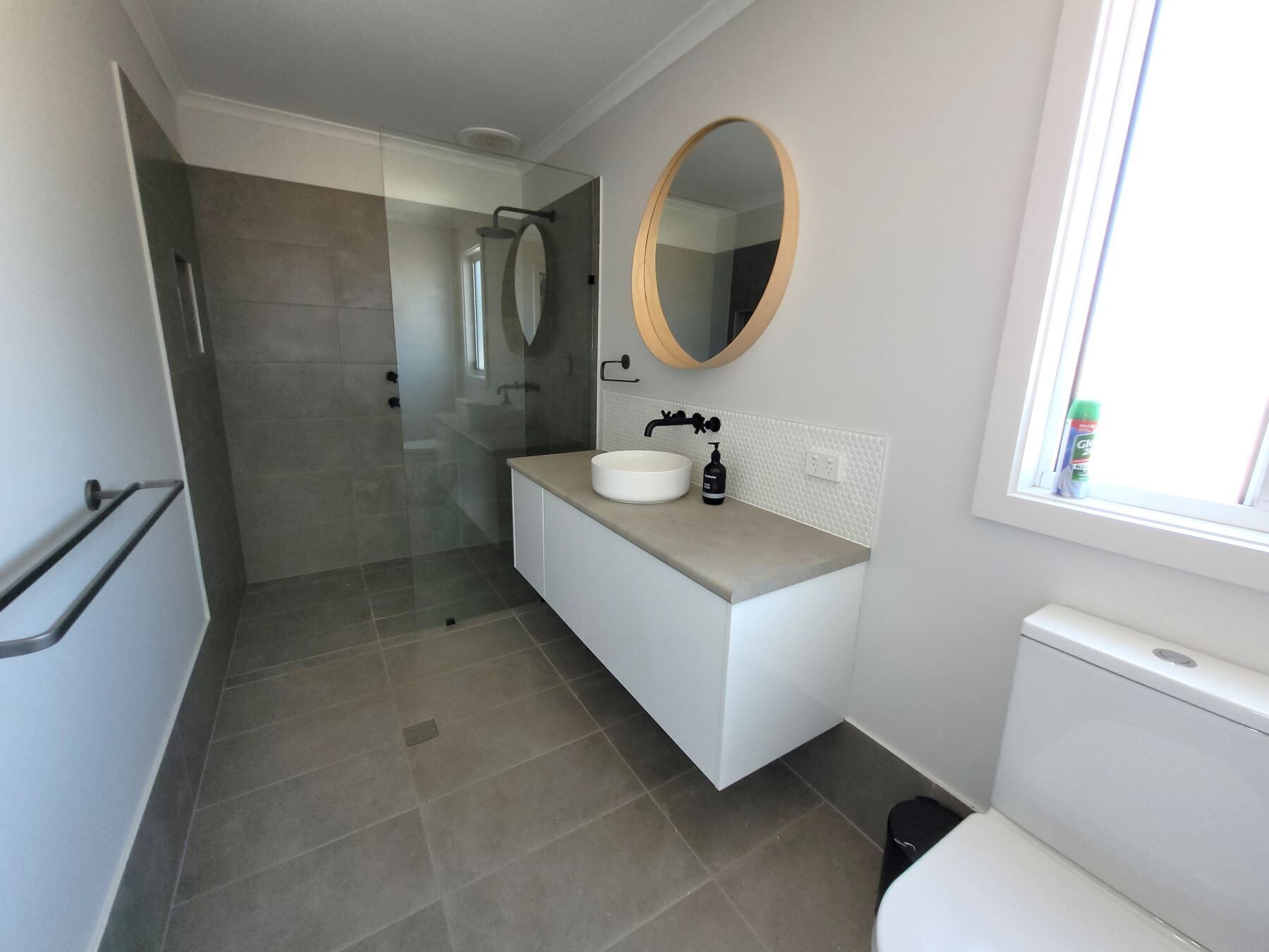 A modern bathroom with a glass shower enclosure, a round mirror, a white sink, and a toilet.