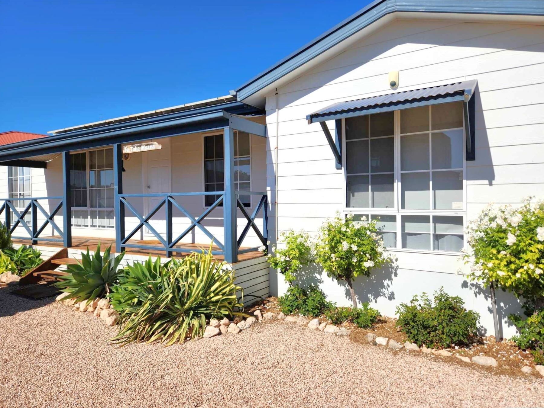A white building with a blue porch and a small garden area with plants and rocks.