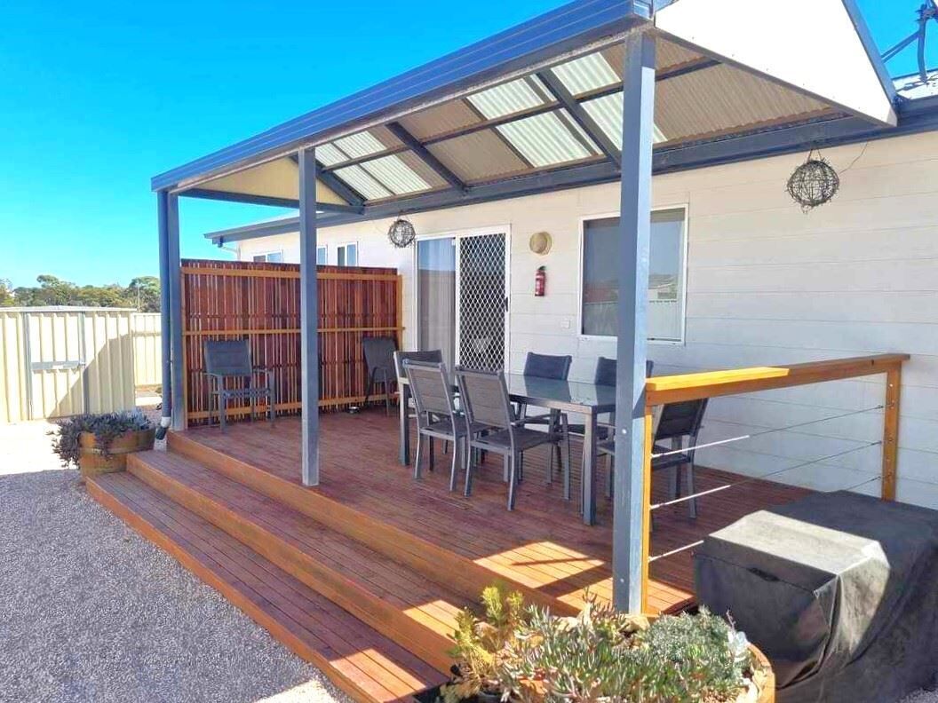 A covered outdoor patio with wooden flooring, a seating area with chairs and a table, and a small grill.