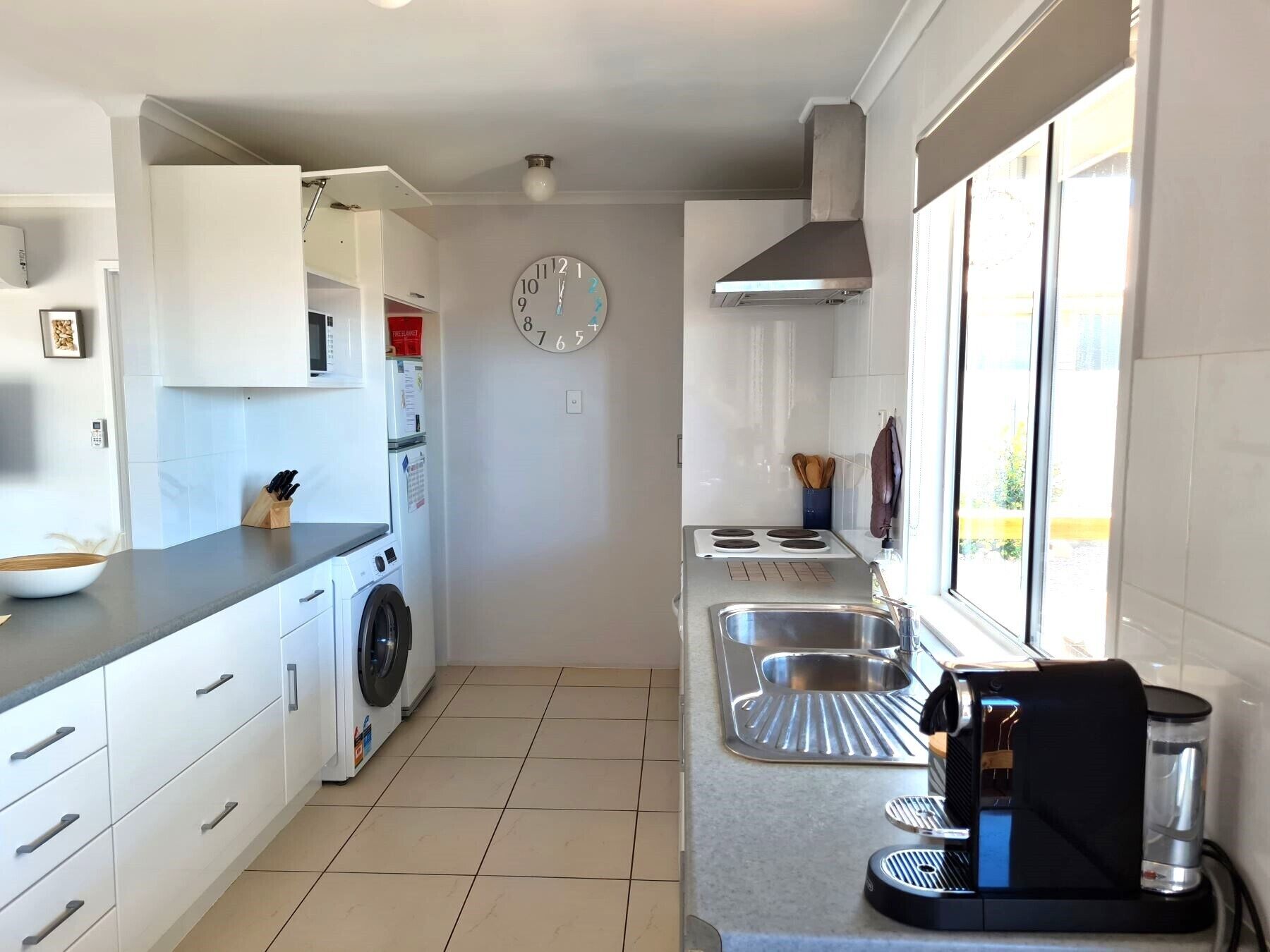 Una cocina moderna con armarios blancos, lavadora integrada, estufa y cafetera.