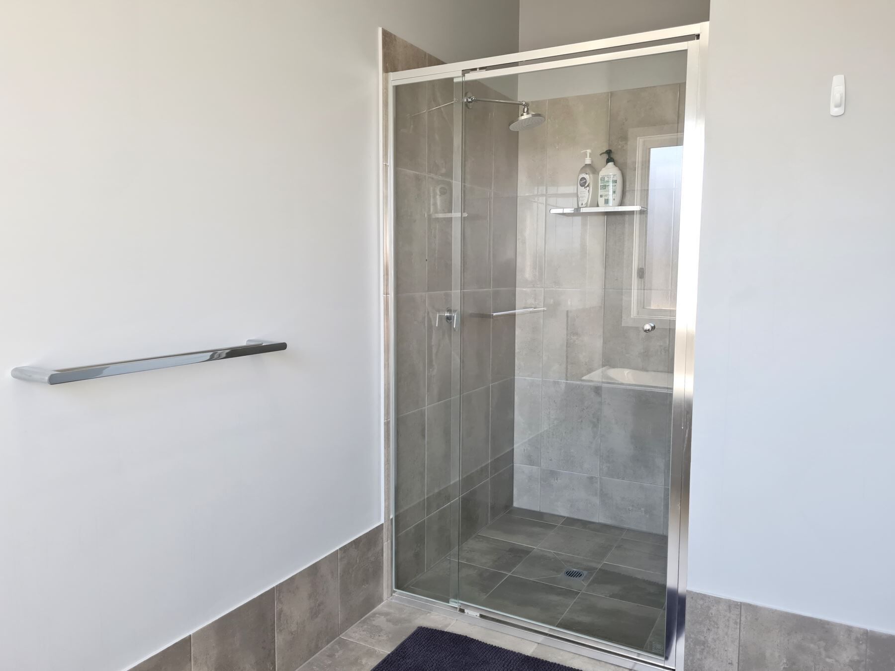Un baño moderno con cabina de ducha de vidrio, un lavamanos blanco y un estante pequeño con artículos de tocador.