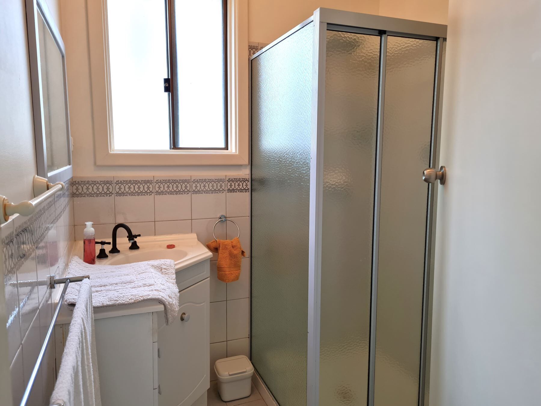 A bathroom with a white sink, a glass shower enclosure, and a window above the sink.