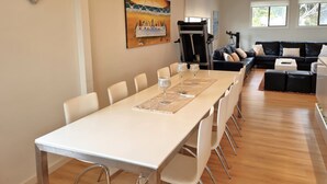 Un espace repas moderne avec une longue table, des chaises blanches et un tableau accroché au mur.