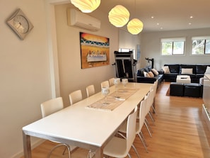 A modern dining area with a long table, white chairs, and a painting on the wall. - Seaside Retreat, Black Point (Black Point)