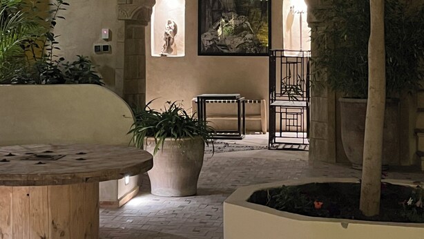 Une cour avec un banc en pierre, des plantes en pot et une statue.