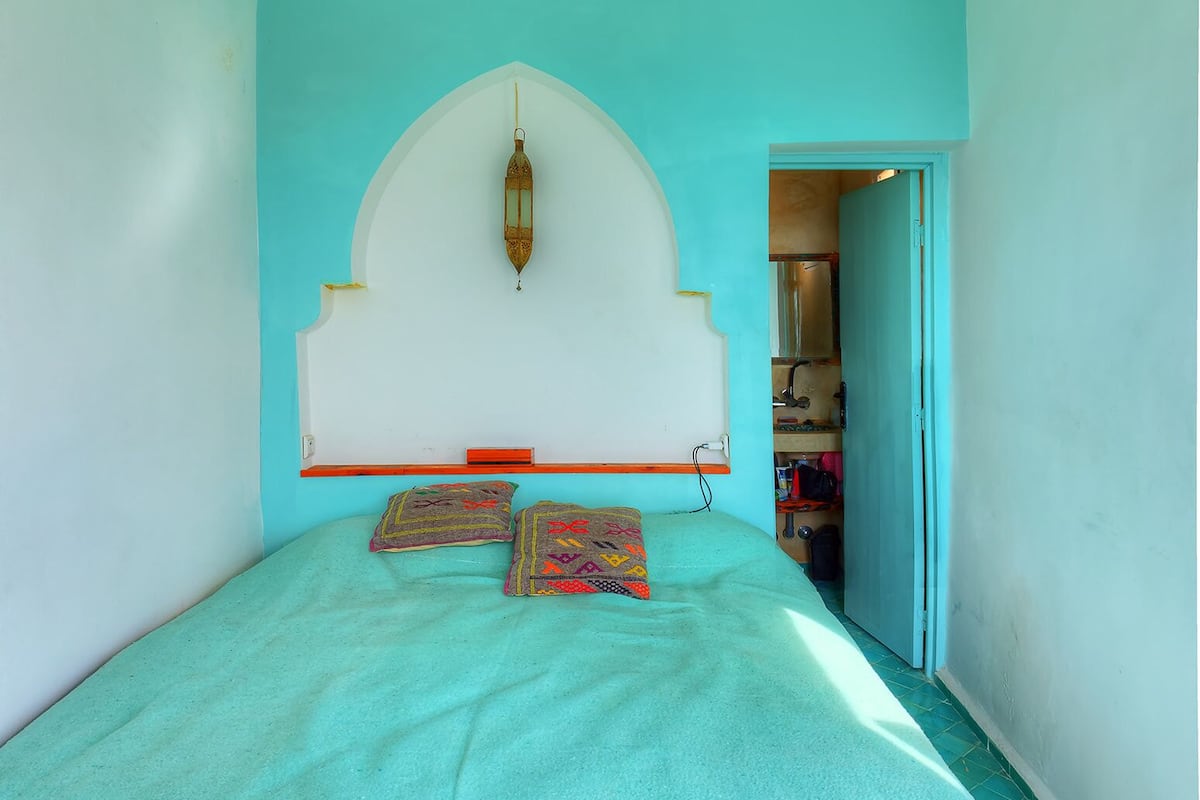 A room with a turquoise wall, a white headboard, and two patterned pillows.