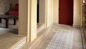 Un couloir orné d’arches, une porte rouge, des carreaux décoratifs et un luminaire suspendu.