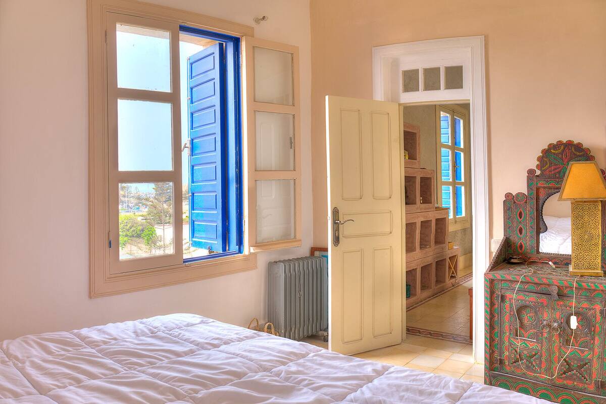 A bedroom with a bed, a radiator, a wardrobe, and a window with blue shutters.