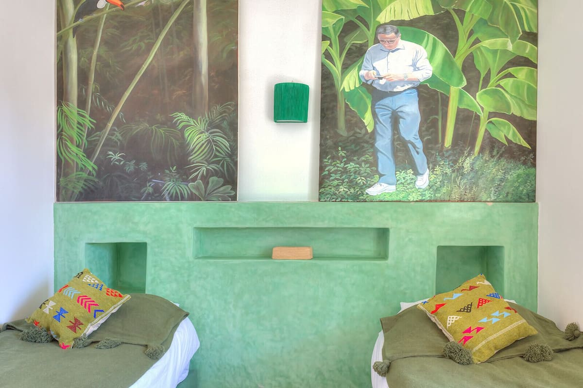A room with two beds, a green headboard, and two large paintings depicting nature scenes.
