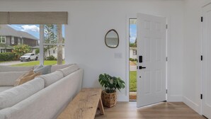 Una sala moderna con un sofá, un banco, una planta en maceta y una puerta que da al exterior.
