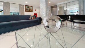 A modern lobby with a glass coffee table, a blue sofa, and a black bench. - Manaíra Palace- LikeHome Hospedagens (João Pessoa)