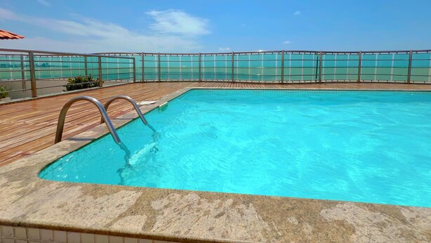 A swimming pool with a wooden deck and a glass barrier. - Manaíra Palace- LikeHome Hospedagens (João Pessoa)