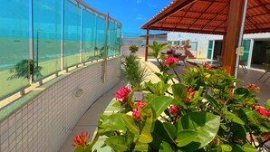 A balcony with a view of a beach and a covered outdoor seating area with chairs and tables. - Manaíra Palace- LikeHome Hospedagens (João Pessoa)