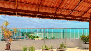 A balcony with a view of a beach and cityscape, featuring potted plants and a tiled floor. - Manaíra Palace- LikeHome Hospedagens (João Pessoa)