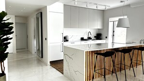 A modern kitchen with white cabinetry, a marble countertop, and black bar stools.