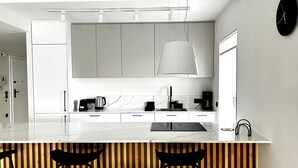 A modern kitchen with white cabinets, a marble countertop, and a wooden dining area.