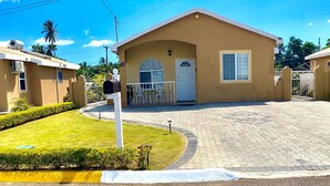 A single-story building with a flat roof, a gated entrance, and a small porch area. - Hidden Gem, Cozy 2-bedroom house with WiFi, AC, Private Pool In Portmore (Portmore)