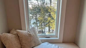 A cozy room with a window seat featuring a patterned throw blanket and fluffy pillows. - The Beach House on Shaws Pond - gorgeous new home directly on the water (New Durham)