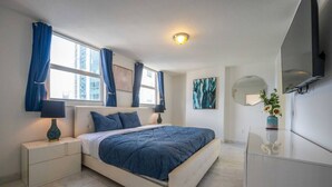 Un dormitorio moderno con una cama grande, una mesita de noche con lámpara, un aparador y un espejo.