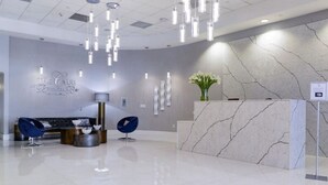 A modern reception area with a marble reception desk, contemporary chairs, and a wall-mounted light fixture. - Amazing spacious unit (Miami)