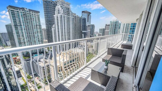 A balcony with wicker furniture and a view of high-rise buildings. - Amazing spacious unit (Miami)