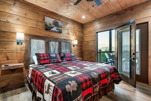 Une chambre confortable avec un plafond en bois, un grand lit recouvert d’une courtepointe, deux lampes fixées au mur et une vue dégagée sur l’extérieur grâce à une porte-fenêtre coulissante.