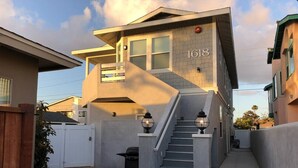 Une maison moderne à deux étages, dont le numéro « 1618 » est clairement visible sur la façade, avec un escalier en béton et un petit espace barbecue extérieur.