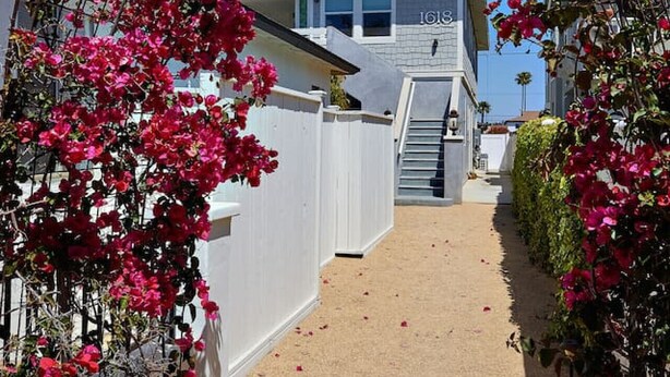 Une allée couverte avec une maison en arrière-plan, entourée de plantes en fleurs.