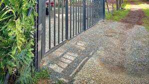 Ein verschlossenes Tor mit einem Kiesweg, der zu einem geparkten Fahrzeug führt.