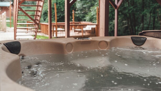 Un jacuzzi con una terraza de madera y mobiliario exterior al fondo.