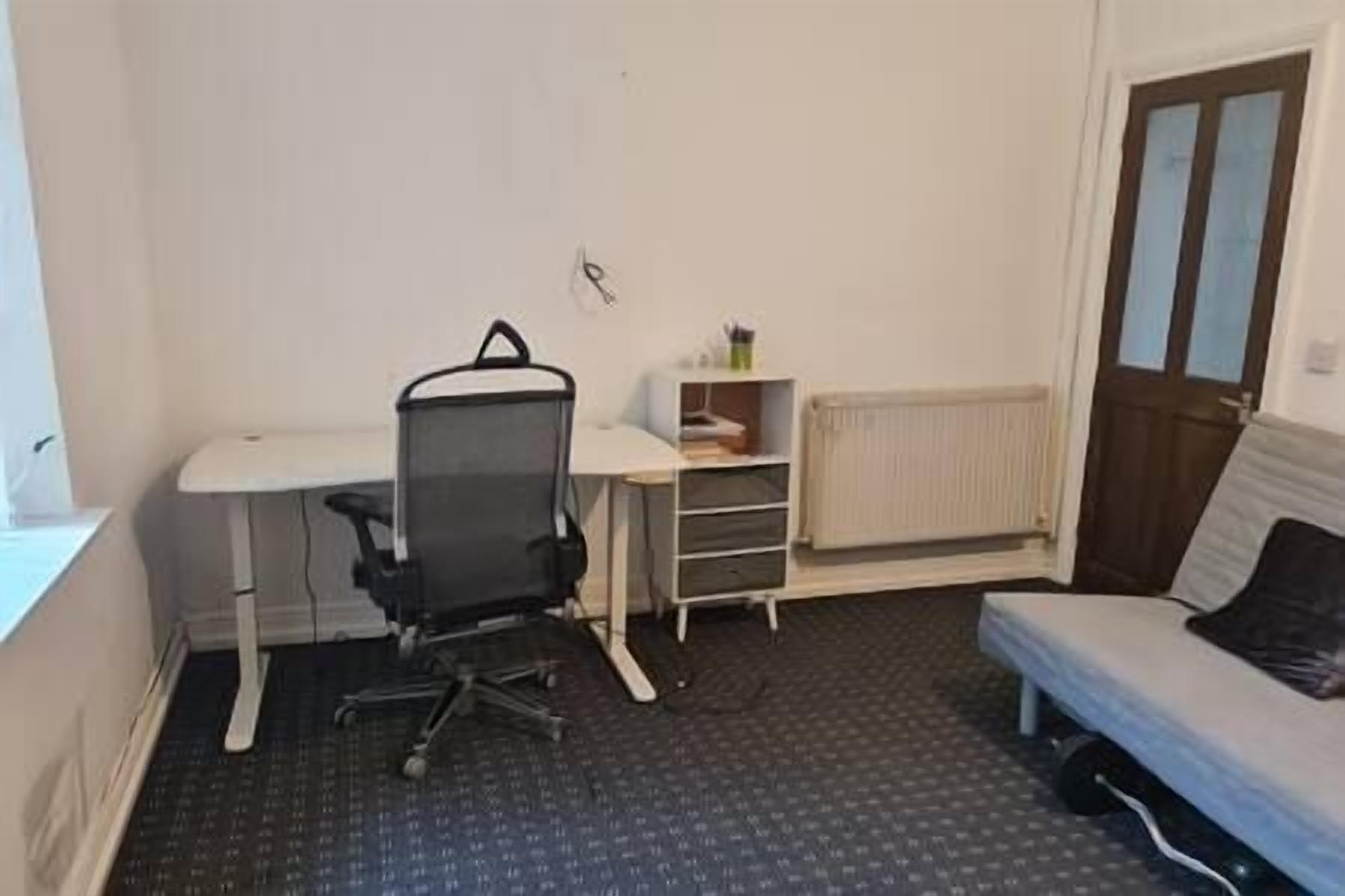 Een kleine, eenvoudig ingerichte kamer met een bureau, stoel en bed.