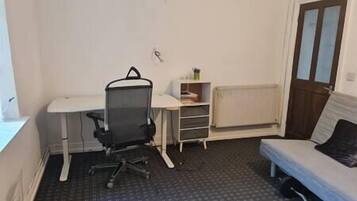 Een kleine, eenvoudig ingerichte kamer met een bureau, stoel en bed.