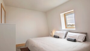 A bedroom with a bed, a bedside table, a lamp, and a window with a view. - Avonside Alpine Estate - Jindabyne (Avonside)